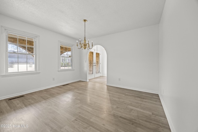 spare room with visible vents, wood finished floors, arched walkways, a notable chandelier, and a textured ceiling