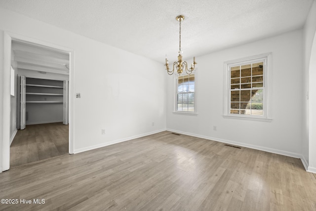 empty room featuring an inviting chandelier, wood finished floors, baseboards, and a textured ceiling