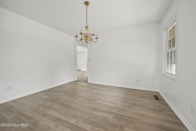 unfurnished dining area featuring an inviting chandelier, wood finished floors, visible vents, and baseboards