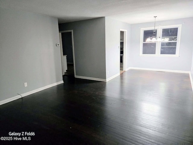 spare room with an inviting chandelier, dark wood-type flooring, and baseboards