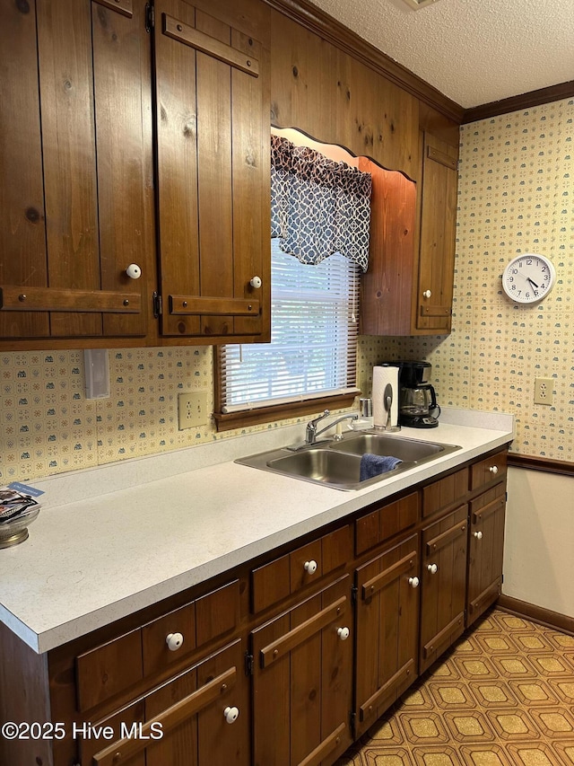 kitchen with a textured ceiling, wallpapered walls, light countertops, and a sink