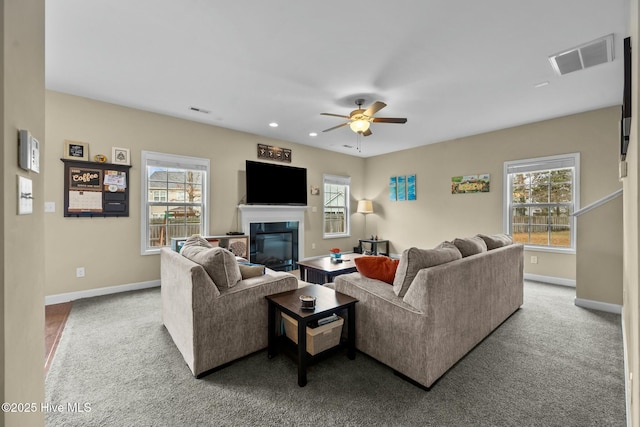 carpeted living area featuring a glass covered fireplace, a ceiling fan, visible vents, and a wealth of natural light