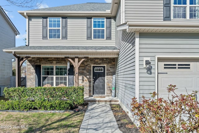 property entrance with stone siding, covered porch, an attached garage, and a shingled roof