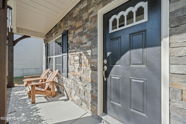 view of exterior entry with a porch and stone siding