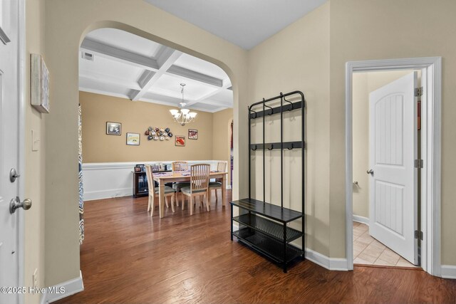 dining area with arched walkways, coffered ceiling, an inviting chandelier, and wood finished floors