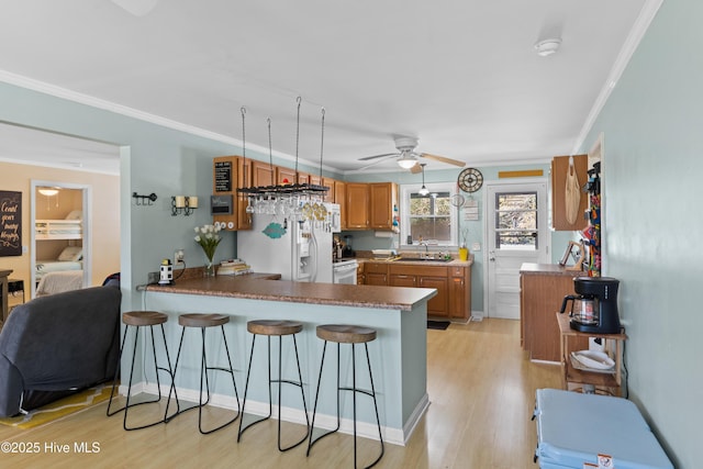 kitchen featuring white appliances, a peninsula, light wood-style floors, ceiling fan, and a sink