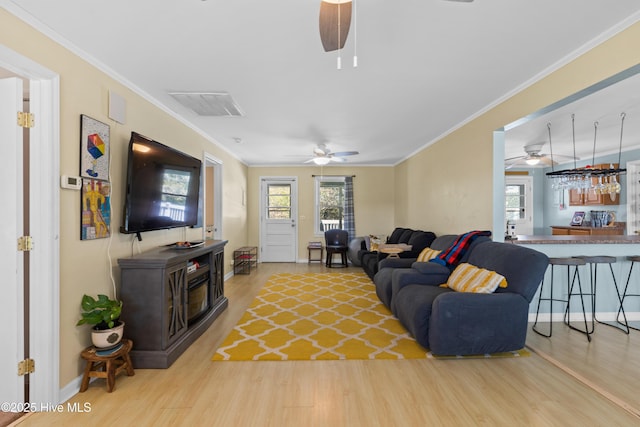 living area featuring ornamental molding, a wood stove, visible vents, ceiling fan, and wood finished floors