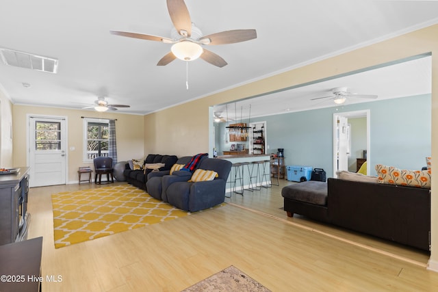 living room featuring visible vents, light wood-type flooring, ornamental molding, and ceiling fan