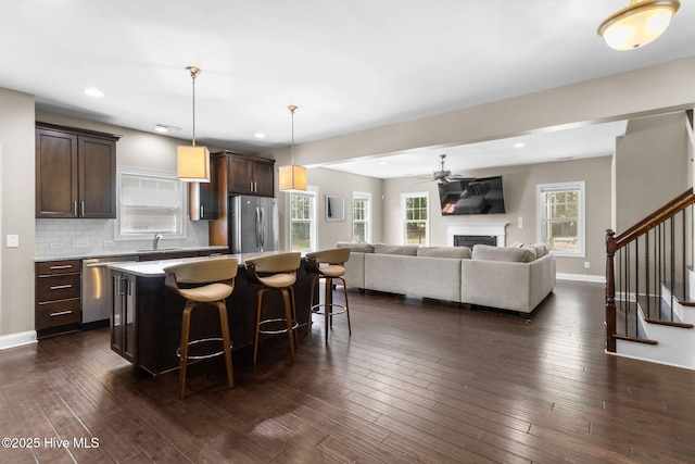 kitchen with dark wood-style floors, a kitchen island, a breakfast bar, stainless steel appliances, and dark brown cabinets