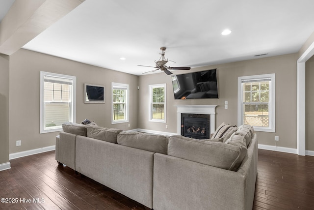 living area with ceiling fan, dark wood-style floors, baseboards, and a glass covered fireplace