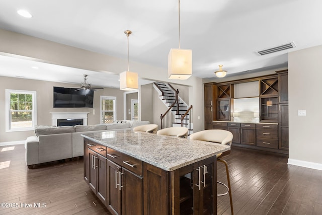 kitchen featuring a ceiling fan, visible vents, baseboards, a fireplace, and dark wood-style flooring