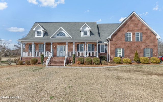 view of front facade featuring brick siding, covered porch, a front yard, and a shingled roof