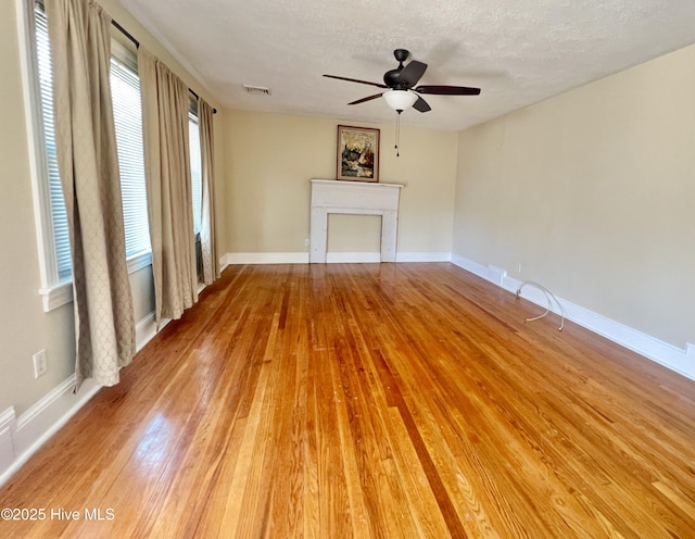 unfurnished living room with visible vents, light wood-style flooring, a fireplace, a textured ceiling, and a ceiling fan