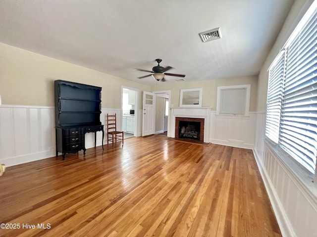 unfurnished living room featuring visible vents, a wainscoted wall, a ceiling fan, light wood-style floors, and a fireplace