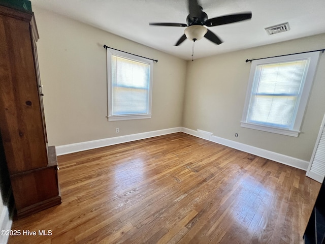 empty room with hardwood / wood-style floors, baseboards, visible vents, and ceiling fan