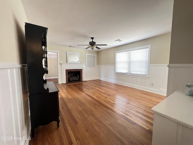 living area featuring visible vents, wainscoting, a ceiling fan, and wood finished floors