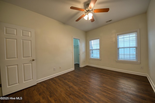 unfurnished bedroom with dark wood finished floors, a walk in closet, baseboards, and visible vents