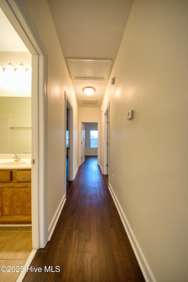 hallway with a sink, visible vents, baseboards, and dark wood-style flooring