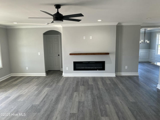 unfurnished living room with a ceiling fan, dark wood finished floors, ornamental molding, wainscoting, and a glass covered fireplace