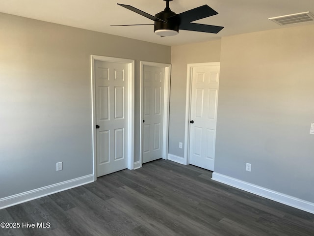 unfurnished bedroom featuring dark wood-style floors, visible vents, a ceiling fan, and baseboards