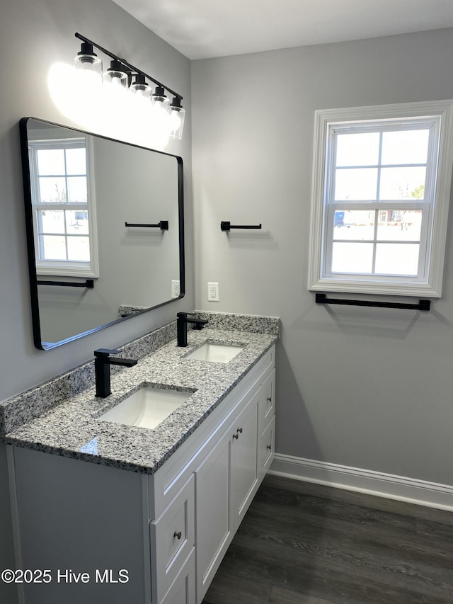 bathroom featuring a sink, baseboards, wood finished floors, and double vanity