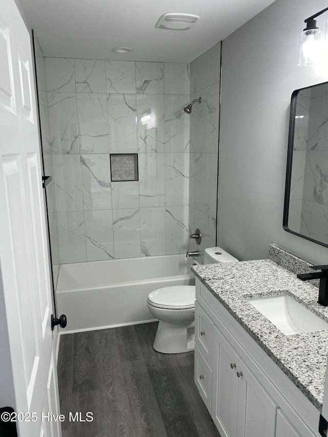 full bath featuring vanity, washtub / shower combination, wood finished floors, visible vents, and toilet