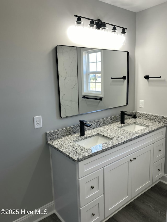 bathroom featuring double vanity, wood finished floors, baseboards, and a sink