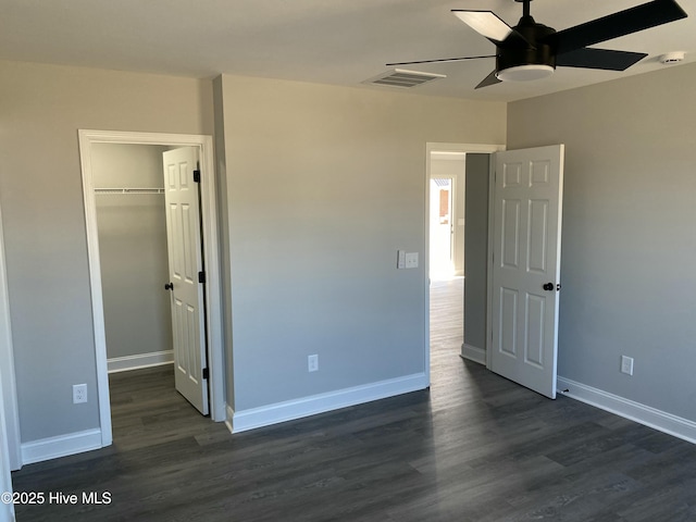 unfurnished bedroom featuring baseboards, a spacious closet, and dark wood-style flooring