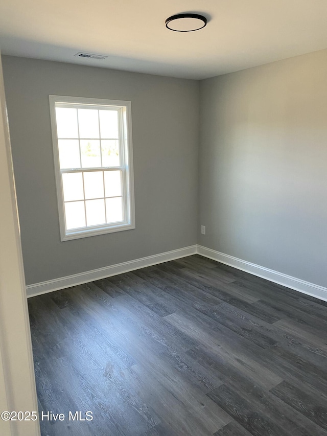 spare room with visible vents, baseboards, and dark wood-type flooring