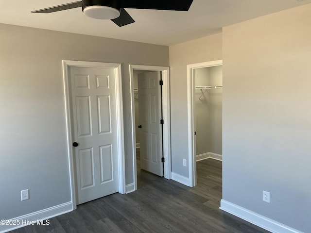 unfurnished bedroom featuring a walk in closet, baseboards, dark wood finished floors, a closet, and a ceiling fan