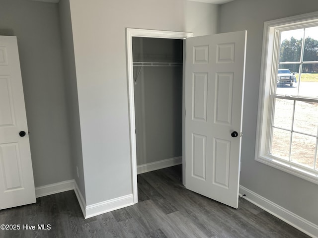 unfurnished bedroom featuring baseboards, multiple windows, a closet, and dark wood-style flooring