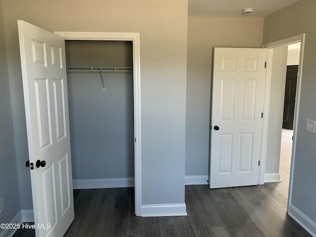 unfurnished bedroom featuring dark wood-type flooring, baseboards, and a closet