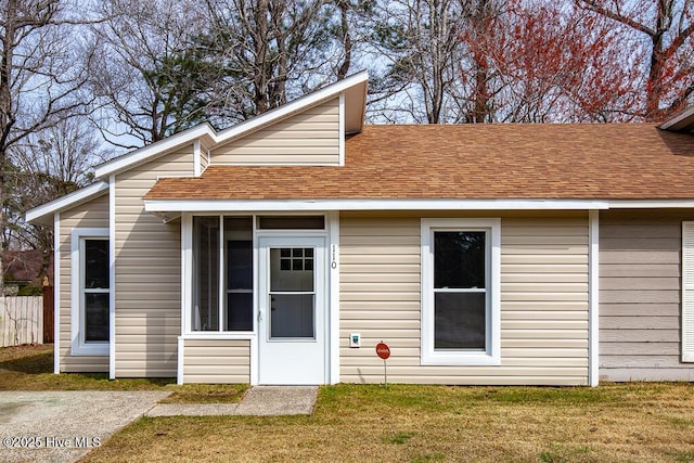 rear view of property featuring a lawn, fence, and a shingled roof