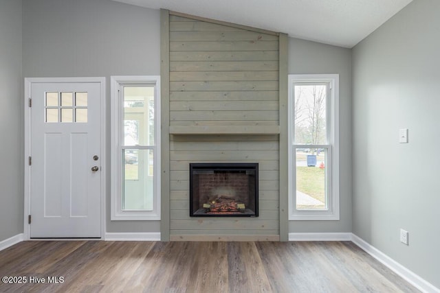 unfurnished living room featuring a fireplace, wood finished floors, baseboards, and vaulted ceiling