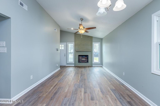 unfurnished living room with wood finished floors, visible vents, baseboards, ceiling fan with notable chandelier, and a large fireplace