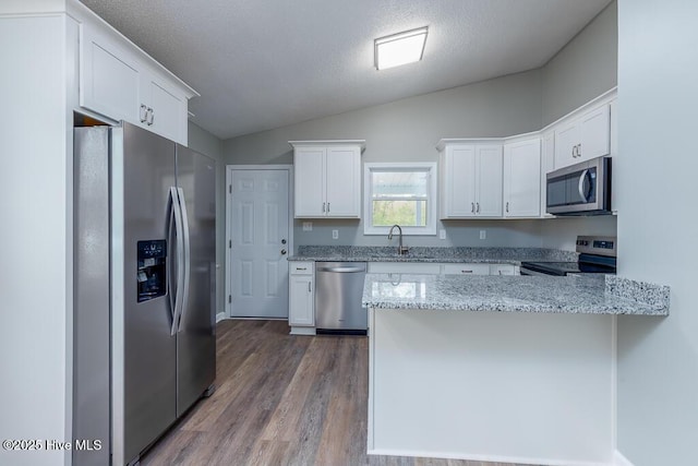 kitchen featuring a sink, white cabinetry, appliances with stainless steel finishes, a peninsula, and vaulted ceiling