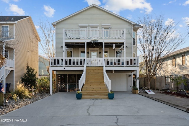 coastal home featuring driveway, stairway, covered porch, an attached garage, and a balcony