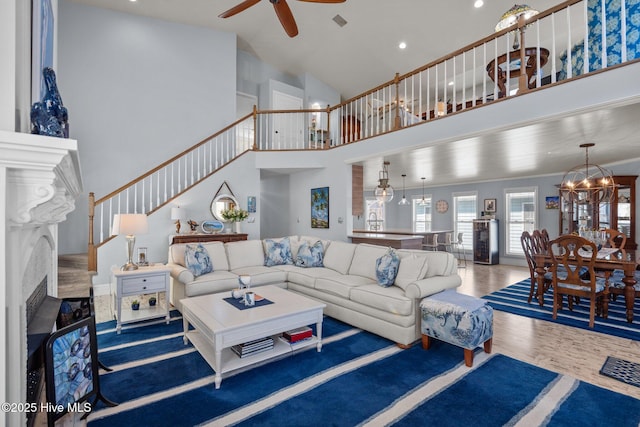 living area featuring stairway, a premium fireplace, ceiling fan with notable chandelier, a towering ceiling, and wood finished floors