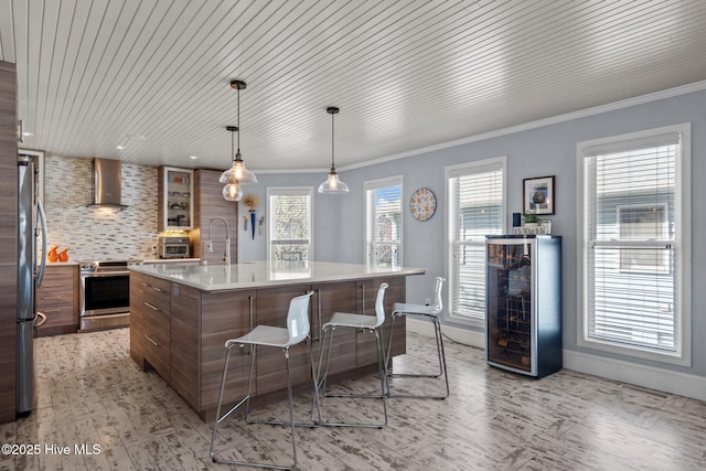 kitchen featuring wall chimney range hood, wine cooler, light countertops, decorative backsplash, and appliances with stainless steel finishes