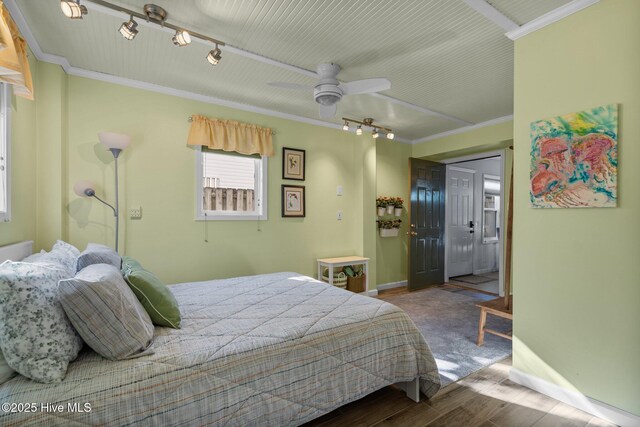 bedroom with rail lighting, crown molding, baseboards, and wood finished floors