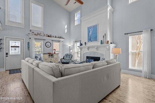 living area with baseboards, a large fireplace, high vaulted ceiling, and wood finished floors