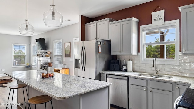 kitchen featuring light stone counters, decorative backsplash, stainless steel appliances, and a sink