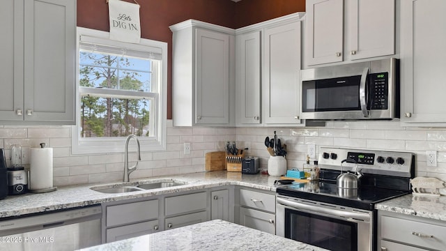 kitchen with light stone counters, decorative backsplash, appliances with stainless steel finishes, and a sink