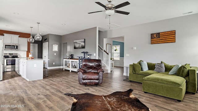 living area with ceiling fan, visible vents, wood finished floors, and stairs