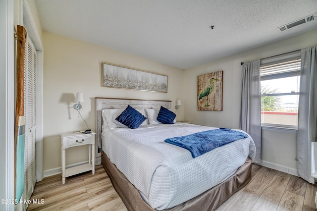 bedroom featuring visible vents, a textured ceiling, baseboards, and wood finished floors