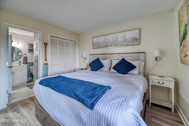 bedroom featuring a closet, ensuite bathroom, baseboards, and wood finished floors