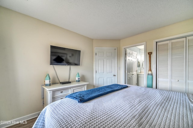 bedroom with wood finished floors, baseboards, ensuite bath, a closet, and a textured ceiling