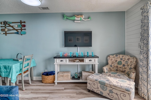 sitting room with visible vents, baseboards, a textured ceiling, and wood finished floors