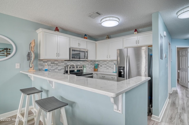 kitchen featuring visible vents, tasteful backsplash, stainless steel appliances, a peninsula, and white cabinets