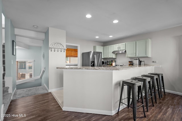 kitchen with dark wood-style floors, under cabinet range hood, stainless steel appliances, baseboards, and a peninsula